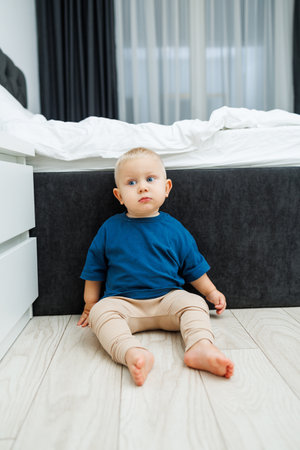 A curious and adorable toddler sits on the floor in a minimalistic room with soft lighting, creating a warm atmosphere that nurtures growth and emotional explorationの写真素材