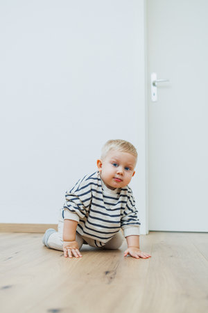 A cheerful baby crawls across a polished wooden floor, showing a playful curiosity in a bright, warm living space that feels comfortable and safe for explorationの写真素材