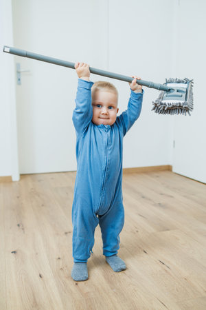 A cheerful toddler raises a colorful cleaning tool, showing playful determination in a stylish, minimalist room filled with natural light, creating a delightful sceneの写真素材