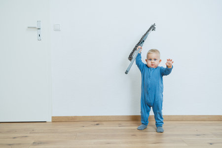 A cheerful and playful toddler wearing a bright blue jumpsuit eagerly lifts a colorful toy, radiating pure joy in a minimalist room adorned with warm wood flooringの写真素材