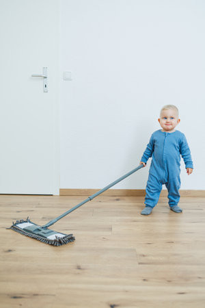 A joyful toddler in a bright blue onesie plays and happily helps with chores, showcasing early learning and delightful family bonding moments filled with happinessの写真素材