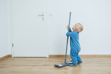 A cheerful and playful toddler joyously mops the floor, showcasing their boundless curiosity and innocence within a bright, clean, and inviting space filled with warmth and joyの写真素材