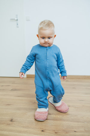 A cheerful toddler happily walks around in a cute and stylish blue onesie accompanied by fluffy pink slippers, truly embodying joy and playfulness in a cozy indoor settingの写真素材