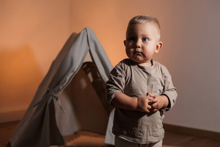 Charming portrait of a toddler standing confidently in front of a soft-colored play tent, capturing a moment of innocence and curiosity in a warm, inviting atmosphere.の写真素材