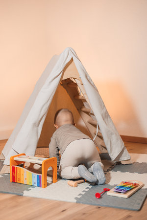 A curious baby crawls into a cozy indoor tent, surrounded by colorful toys and musical instruments, perfect for imaginative play and early development activities.の写真素材