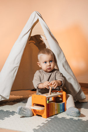 A joyful toddler explores a colorful xylophone in a cozy play tent, embodying the happiness of early childhood play in a nurturing environment that encourages growthの写真素材