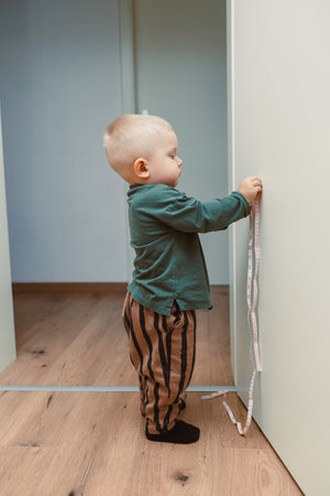 A spirited toddler holds a colorful measuring tape by a modern wall, capturing a delightful moment of exploration and playful learning, showcasing their curiosityの写真素材