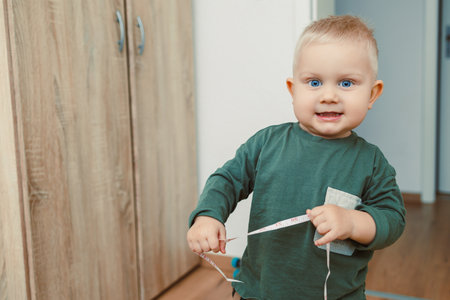 In a snug and cozy interior, a happy toddler is joyfully playing with a bright yellow measuring tape, fully immersed in engaging activities that spark curiosity and playfulnessの写真素材