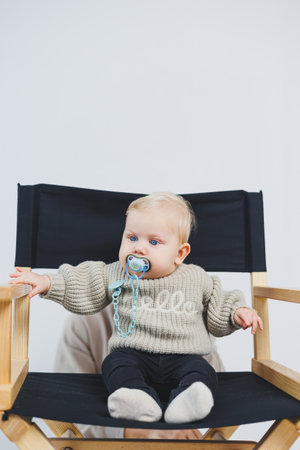 This delightful and charming photo features an adorable baby happily sitting in a directors chair, showcasing their playful innocence, cozy knitwear, and a serene expressionの写真素材