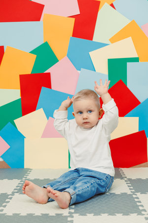 A cheerful baby joyfully sits on a soft, cushioned mat before a beautifully vibrant wall, embodying the essence of joyful innocence and playful discovery, radiating happinessの写真素材