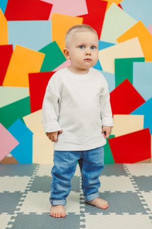 A cute toddler, barefoot in a casual outfit, stands cheerfully against a vibrant backdrop, capturing the essence of innocence and joy in a colorful, playful settingの写真素材