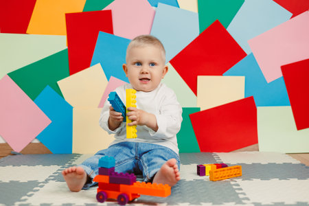 A cheerful little toddler is happily playing with an array of colorful building blocks, joyfully surrounded by whimsical paper cutouts that spark creativity and imaginationの写真素材
