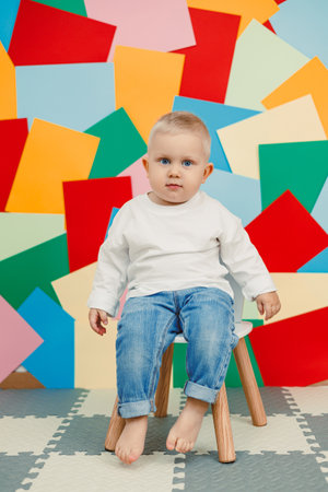 A cheerful toddler sits on a stool, surrounded by colorful paper cutouts, ideal for family or childrens photography that captures childhood innocence and playfulnessの写真素材