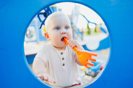 A baby with bright blue eyes joyfully plays and laughs with a vibrant orange toy in a lively, colorful playground, perfectly framed by a cheerful blue circle or backdropの写真素材