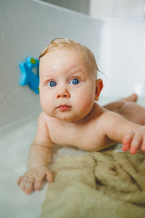 A charming baby relaxes in a warm bath filled with sparkling water, bright blue eyes shining, joyfully playing with colorful bath toys, creating a delightful sceneの写真素材