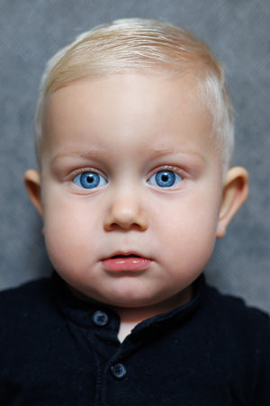 This charming baby portrait showcases striking blue eyes and soft blonde hair against a neutral background, capturing the essence of innocence and curiosity in childrenの写真素材