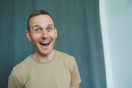 A cheerful young man with radiant blue eyes and a warm, friendly demeanor, radiating joy and enthusiasm as he stands against a simple yet elegant backdrop that enhances his charmの写真素材