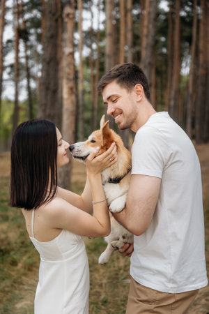 In a serene and peaceful forest, a joyful couple lovingly cradles their adorable corgi, their faces glowing with profound love and happiness amidst the stunning beauty of natureの写真素材