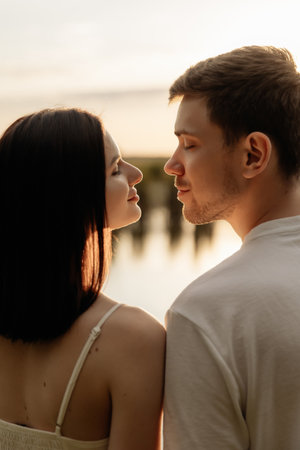 In the sunsets glow, a couple shares an intimate moment. The warm light creates a serene atmosphere, reflecting on calm water, ideal for romance and highlighting their bondの写真素材