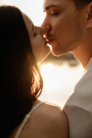 A couple shares a romantic kiss at sunset, framed beautifully by a warm and enchanting glow. This scene is perfect for capturing love, intimacy, and serene moments by the waterの写真素材