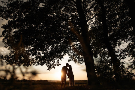 A beautiful silhouette of a couple embracing during sunset, framed by lush trees. Perfect for capturing love, romance, and natures beautyの写真素材