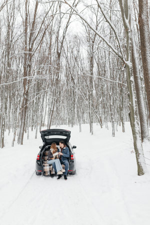 A charming scene of friends gathered at the back of their car in a snowy forest, embracing the beauty of winter while enjoying a cozy and joyful moment together.の写真素材