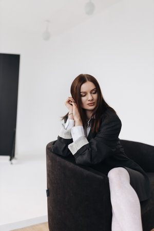 Pretty woman with a square haircut in a black jacket sitting on the floor. Stylish young woman in a white shirt and boots.の写真素材
