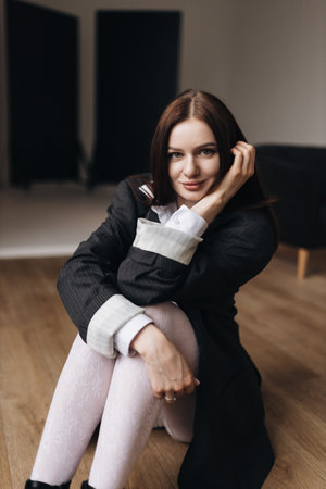 Pretty woman with a square haircut in a black jacket sitting on the floor. Stylish young woman in a white shirt and boots.の写真素材