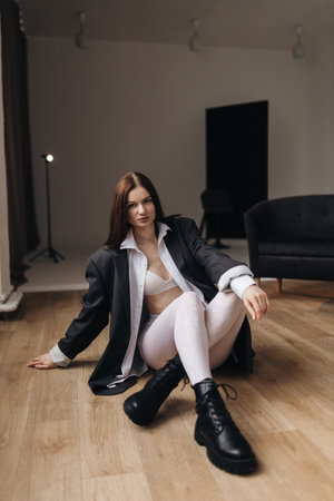 Pretty woman with a square haircut in a black jacket sitting on the floor. Stylish young woman in a white shirt and boots.の写真素材