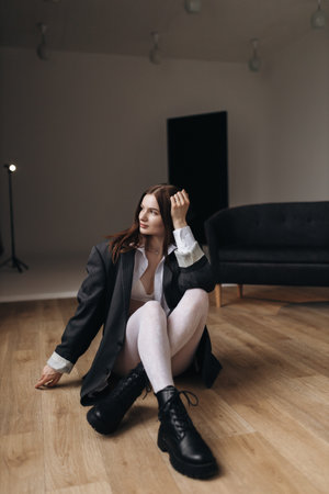 Pretty woman with a square haircut in a black jacket sitting on the floor. Stylish young woman in a white shirt and boots.の写真素材