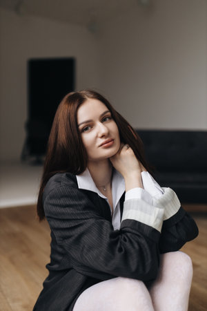 Pretty woman with a square haircut in a black jacket sitting on the floor. Stylish young woman in a white shirt and boots.の写真素材