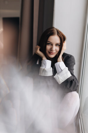 Pretty woman with a square haircut in a black jacket sitting on the floor. Stylish young woman in a white shirt and boots.の写真素材