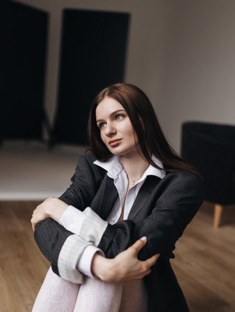 Pretty woman with a square haircut in a black jacket sitting on the floor. Stylish young woman in a white shirt and boots.の写真素材