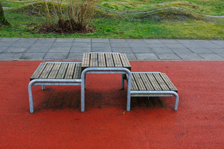 Stylish metal and wood benches have been arranged in a creative layout on a bright red playground...