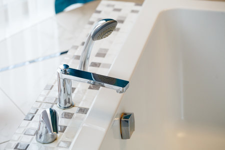 A sleek, shiny chrome faucet elegantly positioned above a luxurious bathtub featuring a modern tile designの写真素材