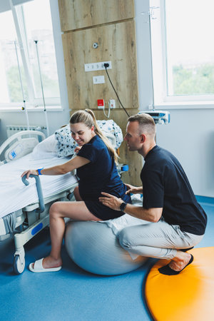 A man supports his wife during childbirth. A woman sits on a fitball during childbirth. A woman goes into labor in the delivery room.の写真素材