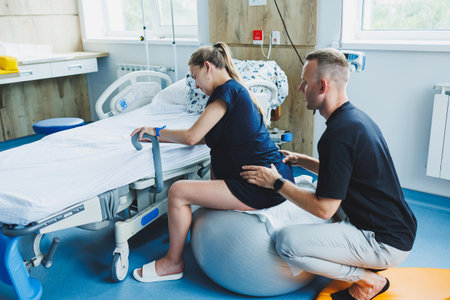 A man supports his wife during childbirth. A woman sits on a fitball during childbirth. A woman goes into labor in the delivery room.の写真素材