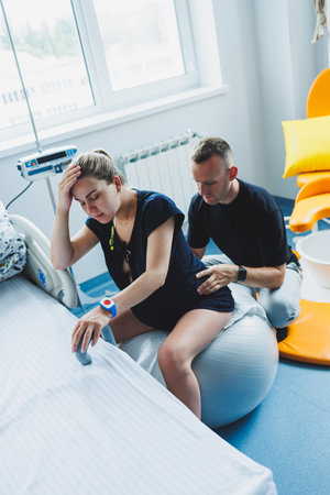 Pregnant woman feels severe pain during childbirth in hospital ward. Caring man helps woman during childbirth and massages her back. Support and love concept.の写真素材