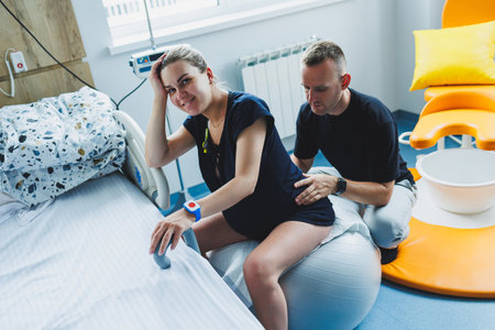 Pregnant woman feels severe pain during childbirth in hospital ward. Caring man helps woman during childbirth and massages her back. Support and love concept.の写真素材