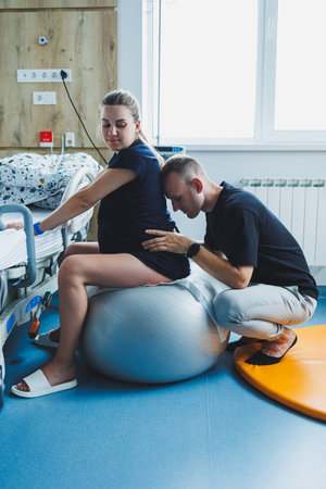 Pregnant woman feels severe pain during childbirth in hospital ward. Caring man helps woman during childbirth and massages her back. Support and love concept.の写真素材