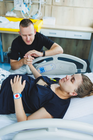 Woman lying feeling pain during childbirth. Pregnancy, childbirth concept. Caring man holding pregnant wife's hand during childbirth. Supportive man helping young woman during childbirth.の写真素材