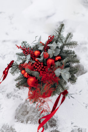 A beautiful winter bouquet with vibrant red ornaments, fresh berries, and frosty greens against a snowy backdrop, perfect for festive decor and joyful celebrationsの写真素材