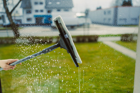 A person diligently uses a squeegee to effectively clean a large window, ensuring a streakfree shine, while bright sunlight significantly enhances the beautiful outdoor viewの写真素材