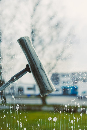 The image shows a squeegee on glass, highlighting the careful window cleaning process in a bright atmosphere that conveys clarity, hygiene, and a sense of sparkleの写真素材