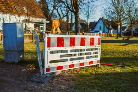 In a sunny neighborhood, a construction barrier with a flashing light indicates ongoing work, ensuring public safety and providing an ideal urban development imageの写真素材