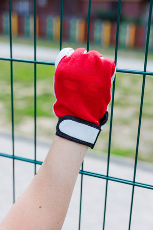 This image shows a vibrant red gloved hand gripping a green metal fence, capturing an energetic moment in an inviting outdoor setting filled with nature's beautyの写真素材