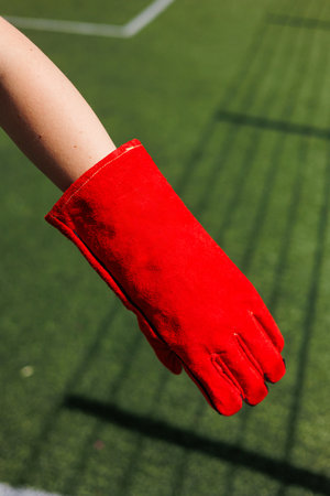A striking red glove on a hand is prominently positioned against a vibrant lush green sports field backdrop, perfect for showcasing athletic gear or various outdoor sports themesの写真素材