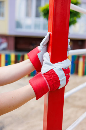 Closeup of gloved hands gripping a bright red gym pole, displaying dedication to strength training and a commitment to a healthy lifestyle in a vibrant outdoor settingの写真素材