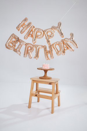 Celebrate joyfully This image features a vibrant Happy Birthday balloon display with a cute cake on a wooden stool, ideal for birthday party themes and decorの写真素材