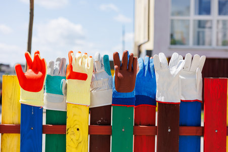 A creative display of colorful gloves mounted on a wooden fence, showcasing a playful visual aesthetic ideal for children's environments and outdoor installations.の写真素材